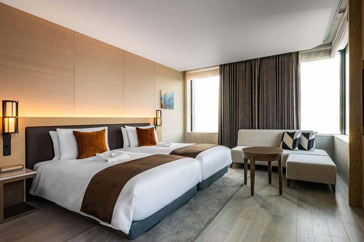 A hotel room with two beds, a sofa, a small table, and a TV.