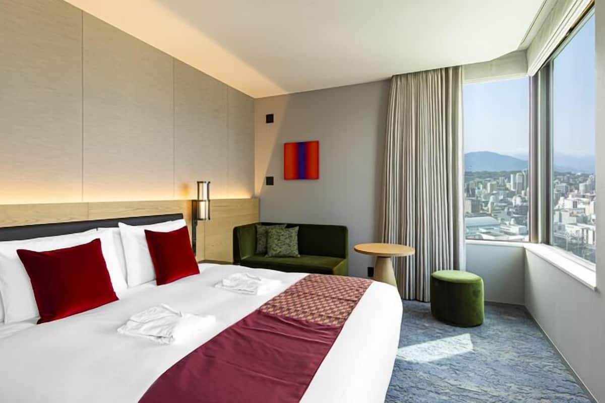 A hotel room with a large bed, a sofa, a small table, and a view of the city.