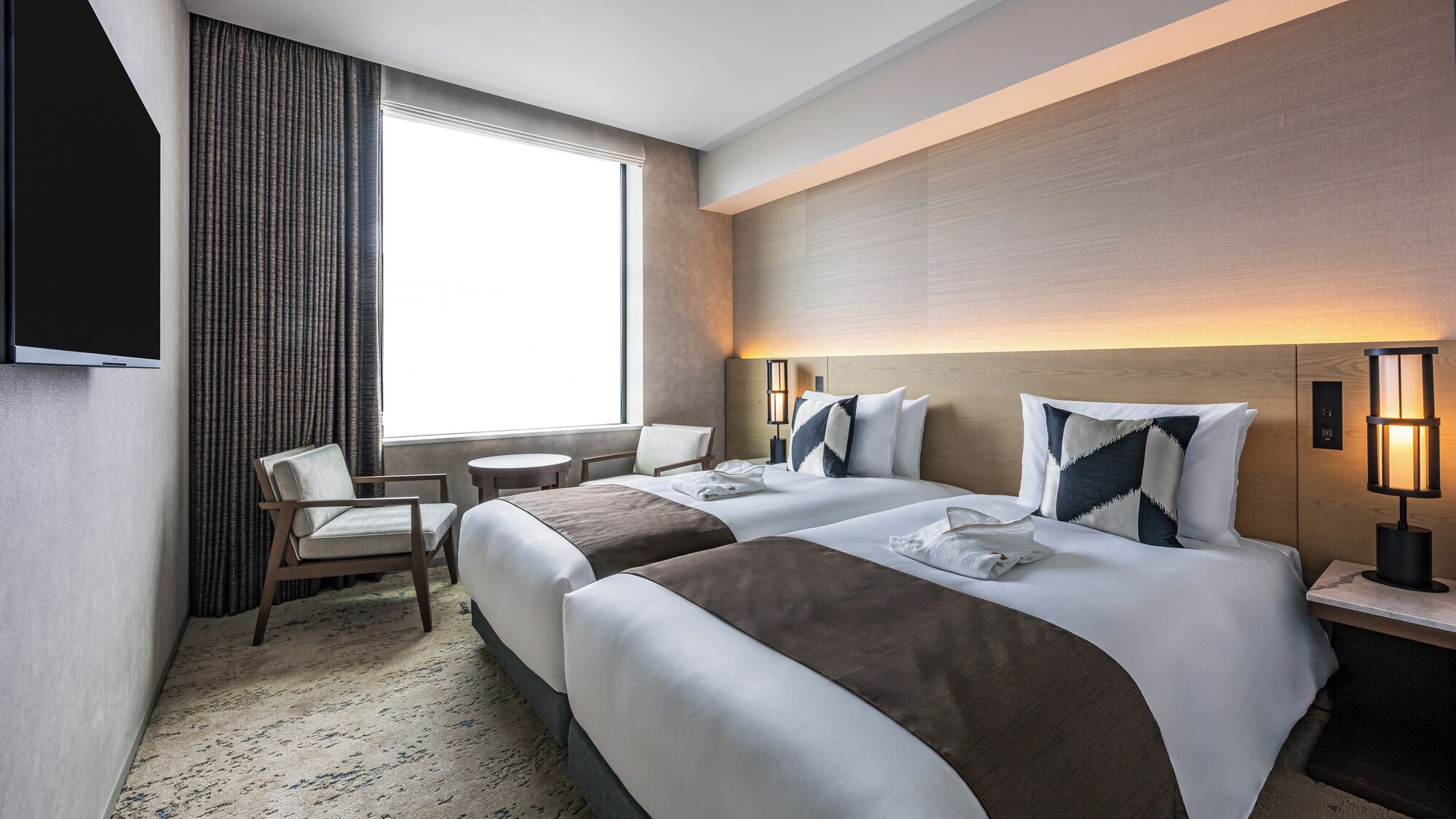 A hotel room with two beds, a TV, a window with curtains, a desk, and a chair.