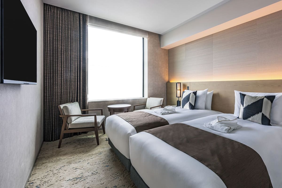 A hotel room with two beds, a TV, a window with curtains, a desk, and a chair.