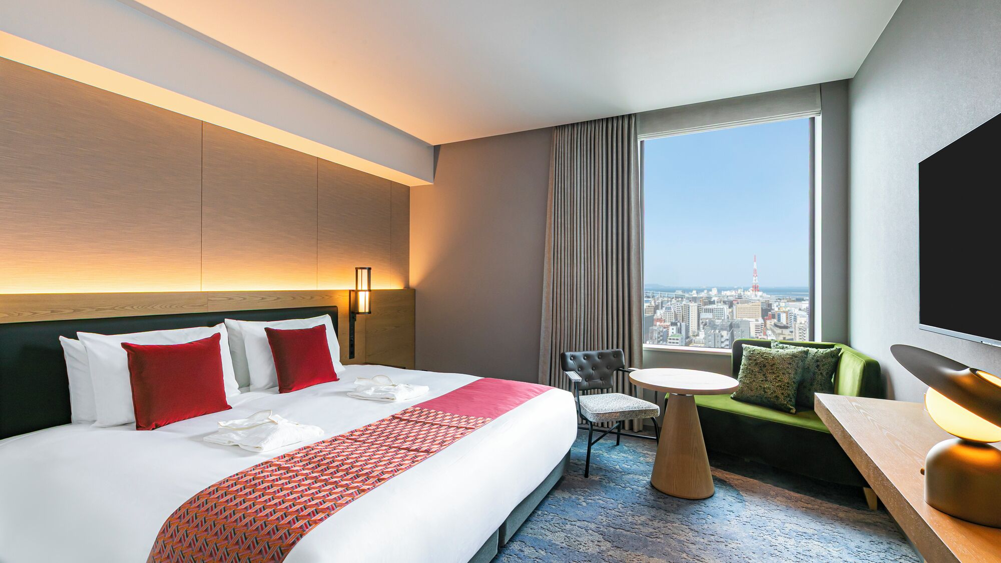 A hotel room with a large bed, a small round table, a sofa, and a TV.