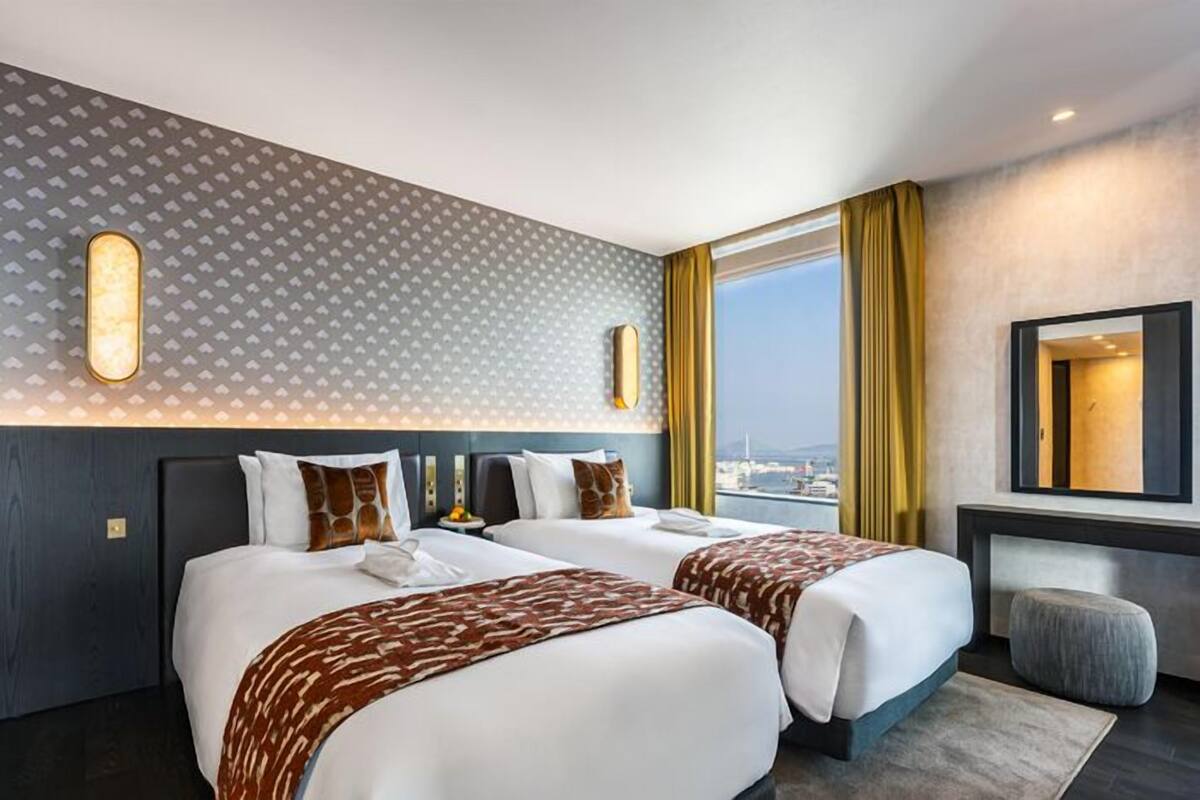 A hotel room with two beds, a large window with a view, a mirror, and a patterned wall.