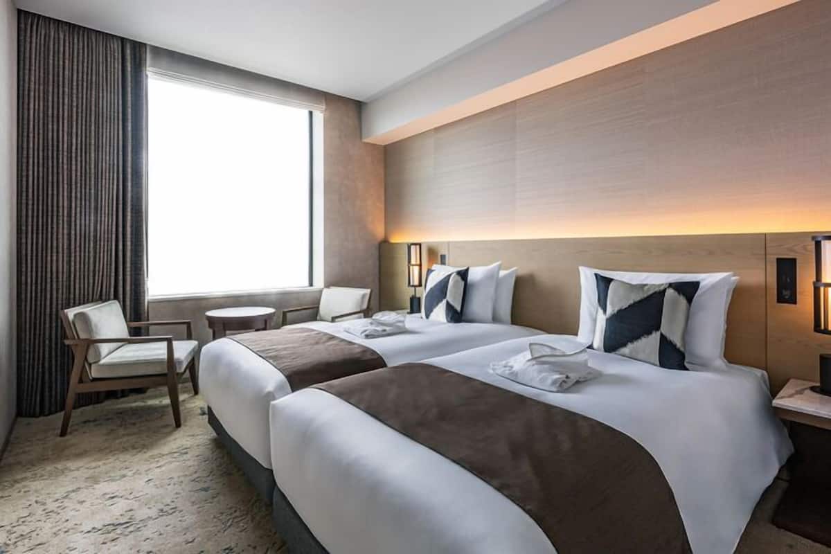 A hotel room with two beds, a TV, a window with curtains, a desk, and a chair.