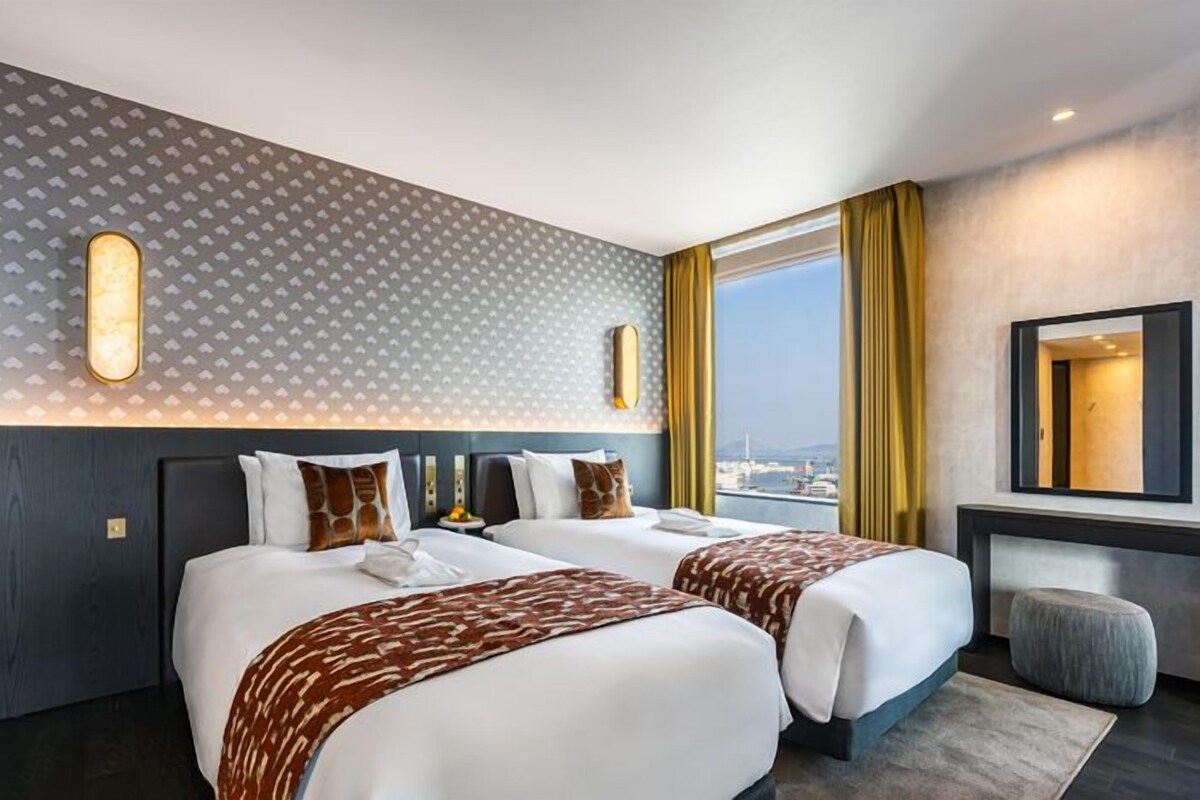A hotel room with two beds, a large window with a view, a mirror, and a patterned wall.