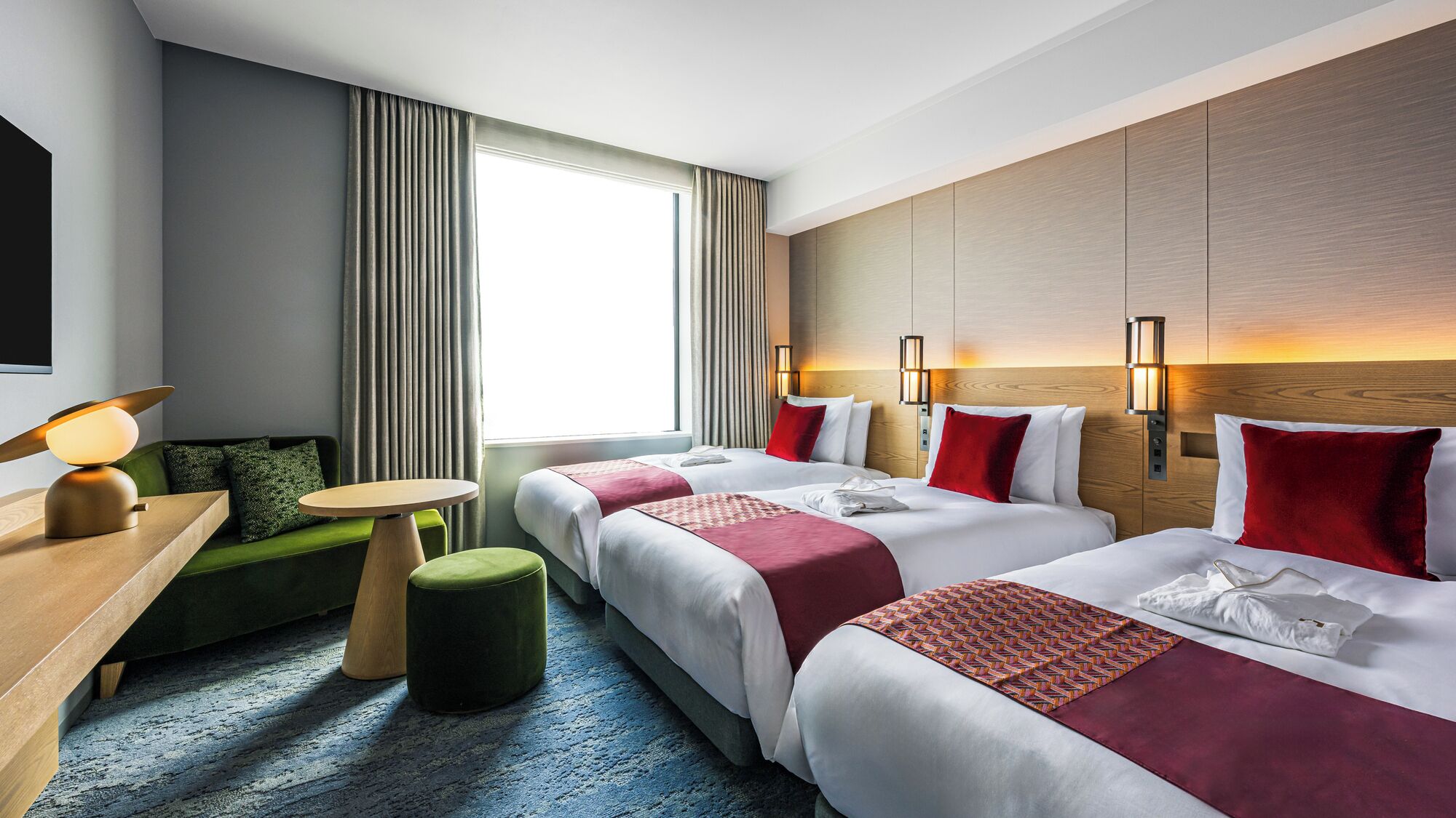 A hotel room with two beds, a desk, a chair, a small table, and a window with curtains.