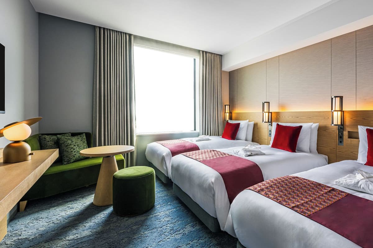A hotel room with two beds, a desk, a chair, a small table, and a window with curtains.