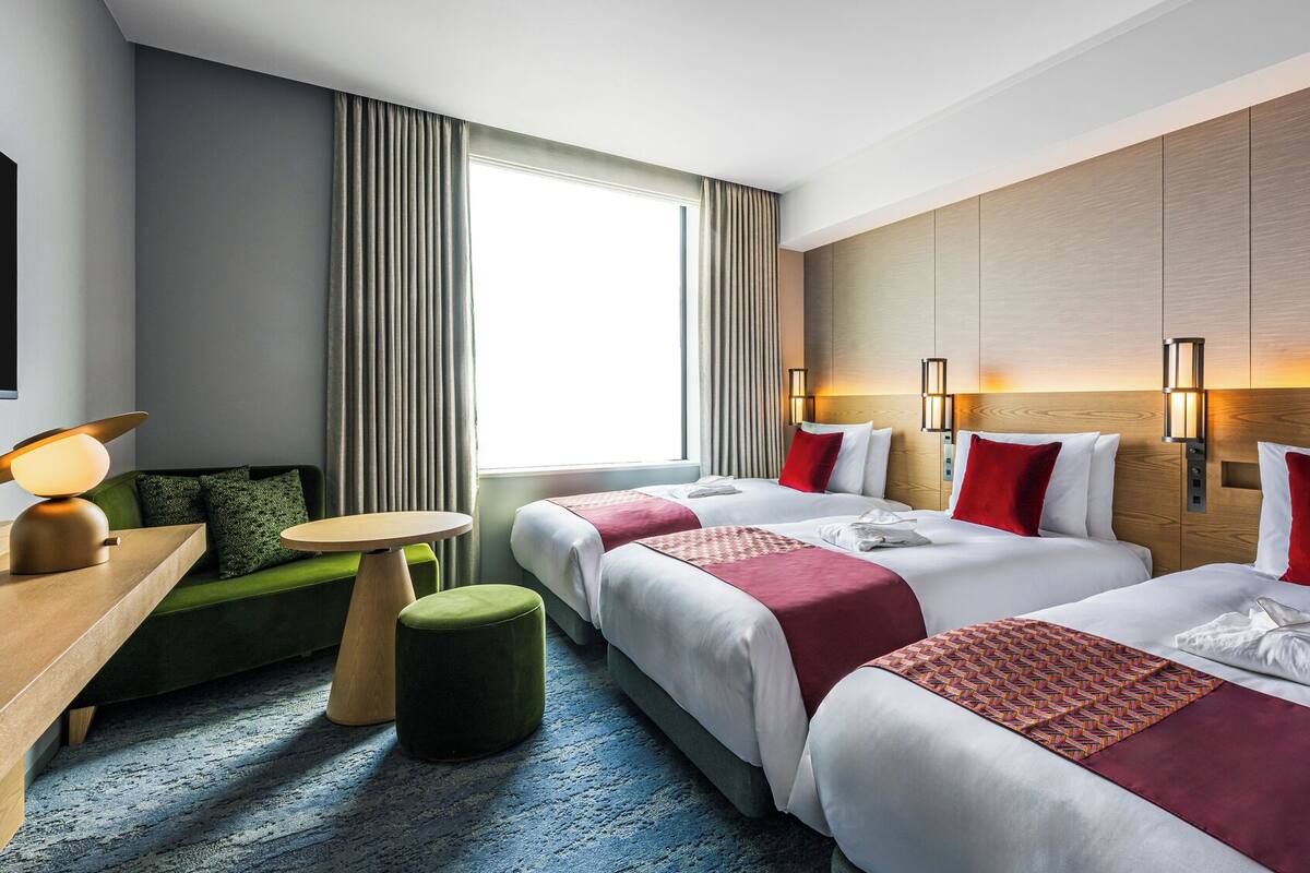 A hotel room with two beds, a desk, a chair, a small table, and a window with curtains.