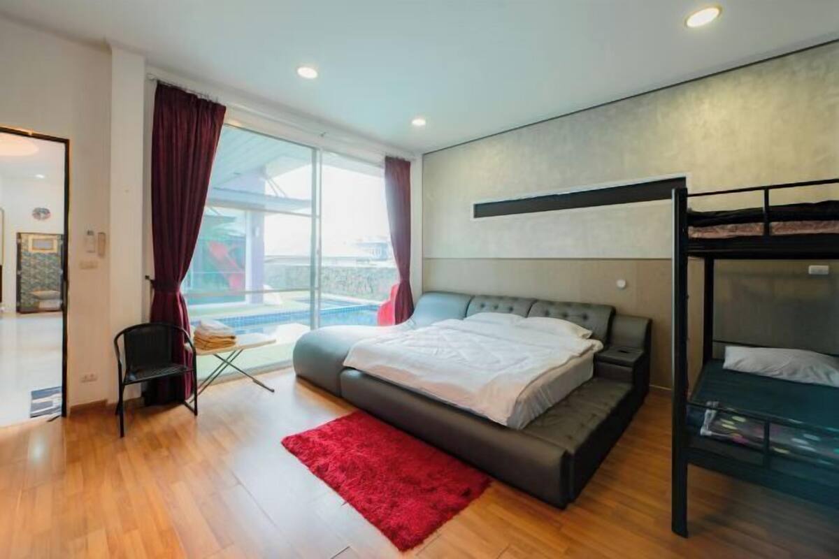 A modern bedroom with a large bed, a bunk bed, a red rug, and a view of the outdoors.