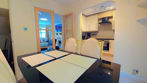 A dining area with a black table and four chairs, a kitchen with white cabinets and a stove, and a door leading to another room.