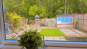 A backyard with a lawn, a wooden fence, a patio table, and a small shed.