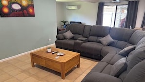 A living room with a sectional sofa, a wooden coffee table, and a painting on the wall. - Family retreat in Caboolture big house (Brisbane)