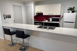 Cocina moderna con armarios blancos, salpicadero rojo, microondas y refrigerador. Hay dos taburetes negros en la isla.