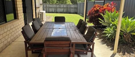 Un patio cubierto con una mesa y sillas de madera, rodeado por un muro de ladrillo y una cerca de madera.