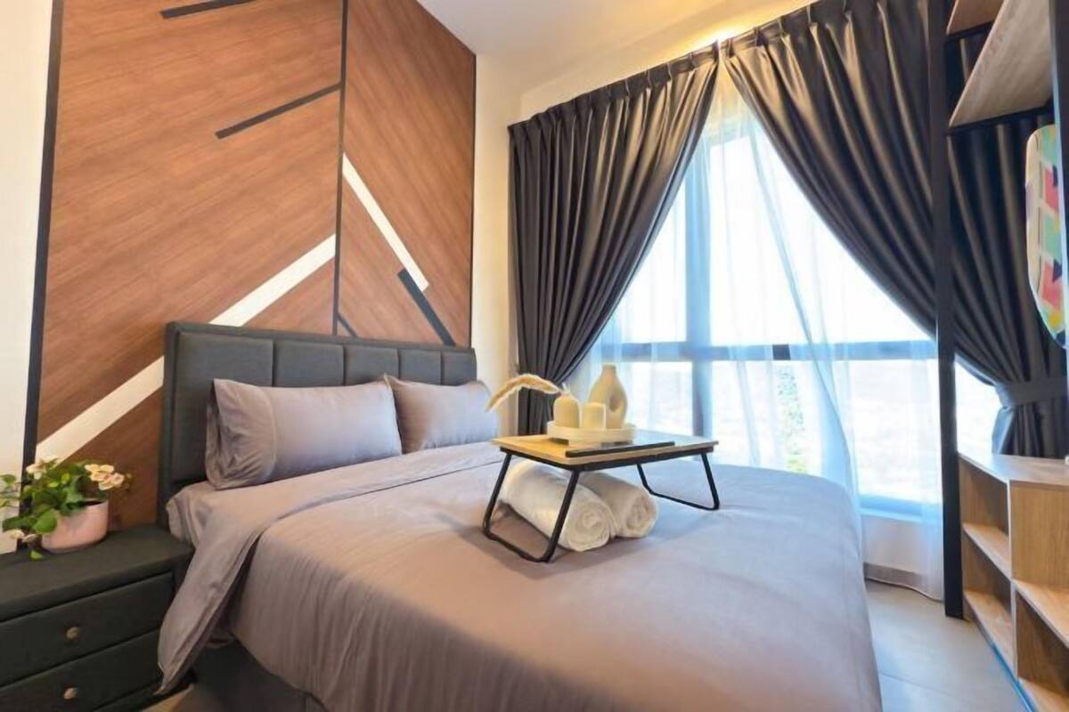 Habitación de hotel moderna con una cama grande, una mesita de noche con lámpara y vistas al exterior a través de amplias ventanas.