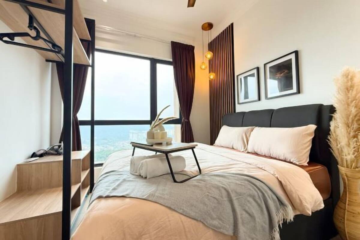 Un dormitorio moderno con cama, una mesita de noche con lámpara, ventana con cortinas y vistas a la ciudad.