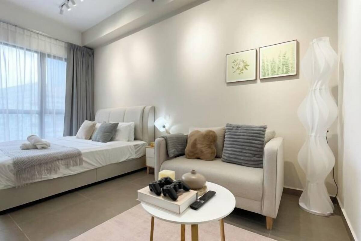 Un dormitorio moderno con una cama, un sofá, una mesita con libros y mandos a distancia, y dos cuadros en la pared.