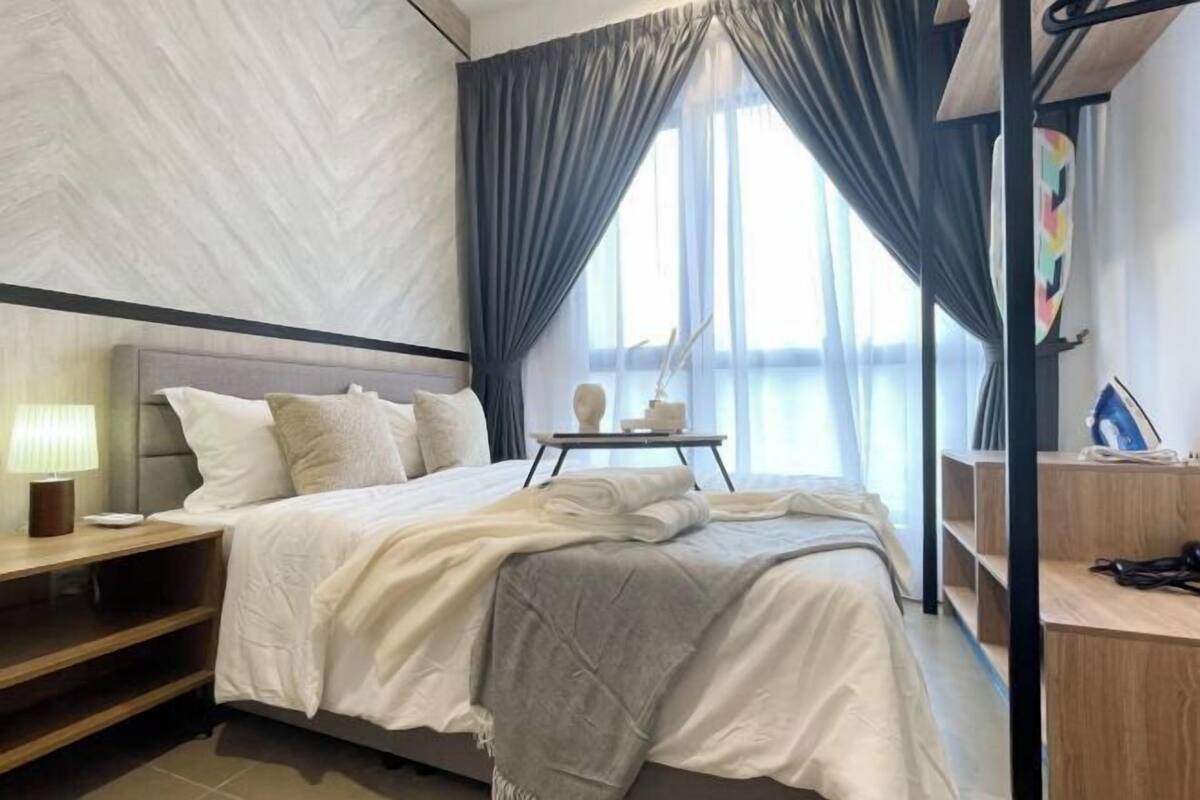 Un dormitorio con cama, mesita de noche, lámpara y vistas al exterior a través de amplias ventanas.