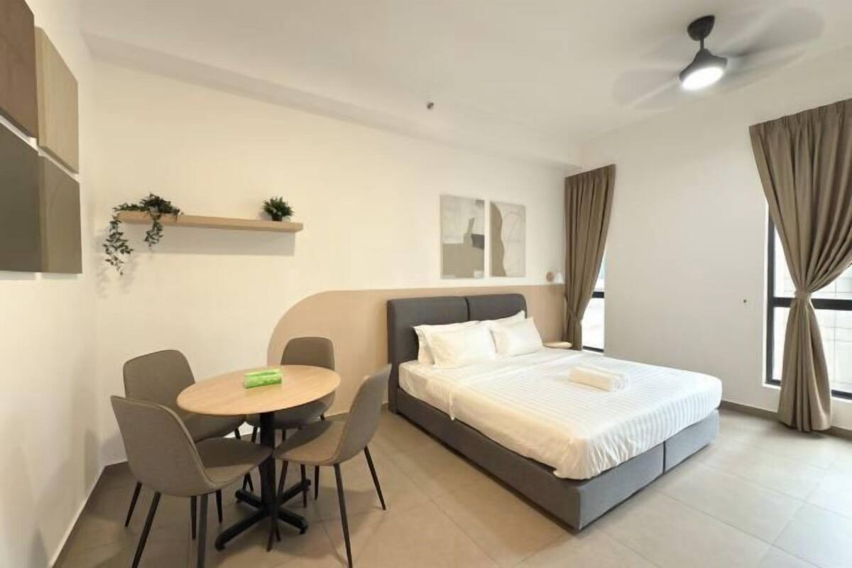 Una habitación de hotel moderna con una cama, una mesa redonda de comedor con sillas, un ventilador de techo y una ventana con cortinas.