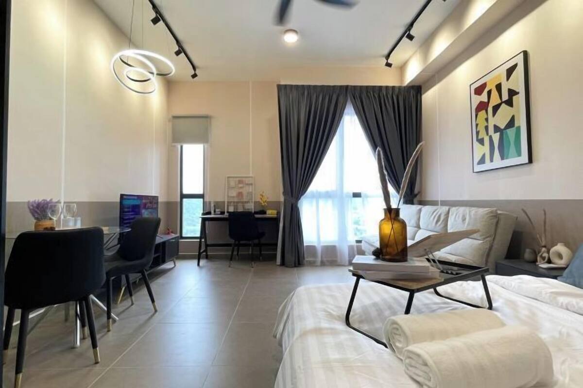Una habitación de hotel moderna con cama, escritorio y silla, un ventanal con cortinas y un cuadro en la pared.
