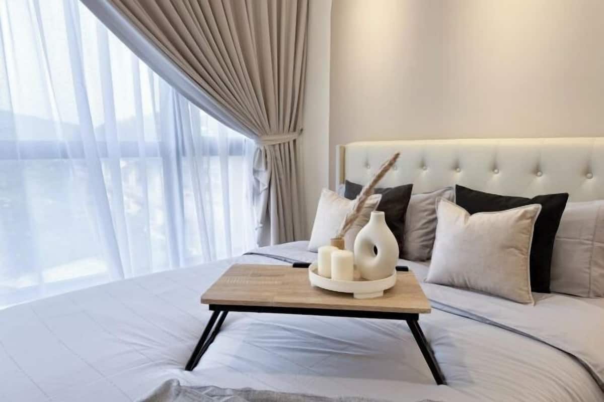 A modern hotel room with a large bed, a bedside table with decorative items, and a view through sheer curtains.