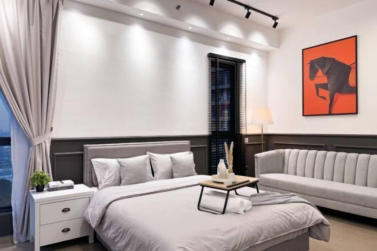 Un dormitorio moderno con cama, mesita de noche, lámpara y sofá.