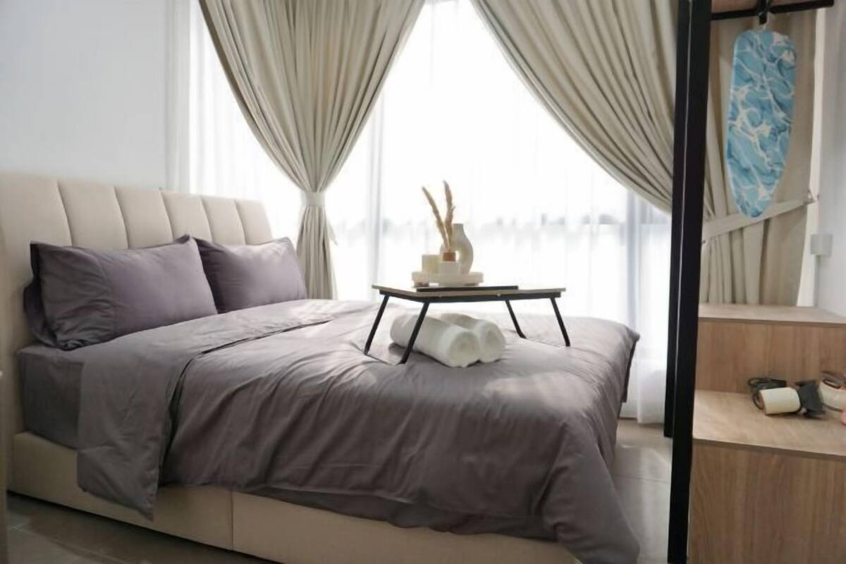 Un dormitorio moderno con una cama grande, una mesita de noche con un florero y toallas enrolladas, y vistas al exterior a través de cortinas translúcidas.