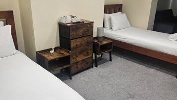 A hotel room with two single beds, a wooden nightstand with a lamp, a small desk with a chair, and a large mirror on the wall.