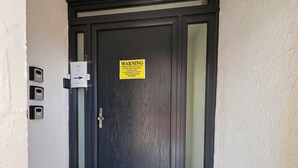 Μια σκούρα ξύλινη πόρτα με μια προειδοποιητική πινακίδα σχετικά με την παρακολούθηση, μια σχισμή για την αλληλογραφία και ένα χαλάκι.