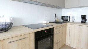 Eine moderne Küche mit hellen Holzschränken, einem schwarzen Backofen, einer Mikrowelle, einer Kaffeemaschine und einer schwarzen Arbeitsplatte.