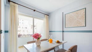 Uma sala de jantar com uma mesa, cadeiras, um vaso de flores, um copo de suco de laranja e uma obra de arte emoldurada na parede.