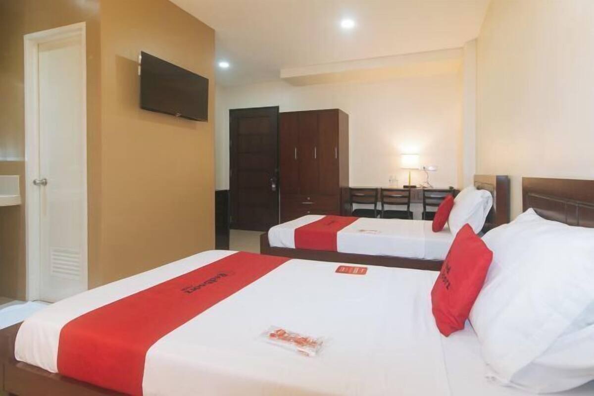 A hotel room with two beds, a television, a desk with a chair, and a wardrobe.