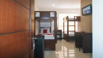 A hotel room with a wooden wardrobe, a bed with a red pillow, a desk, and a television on the wall.