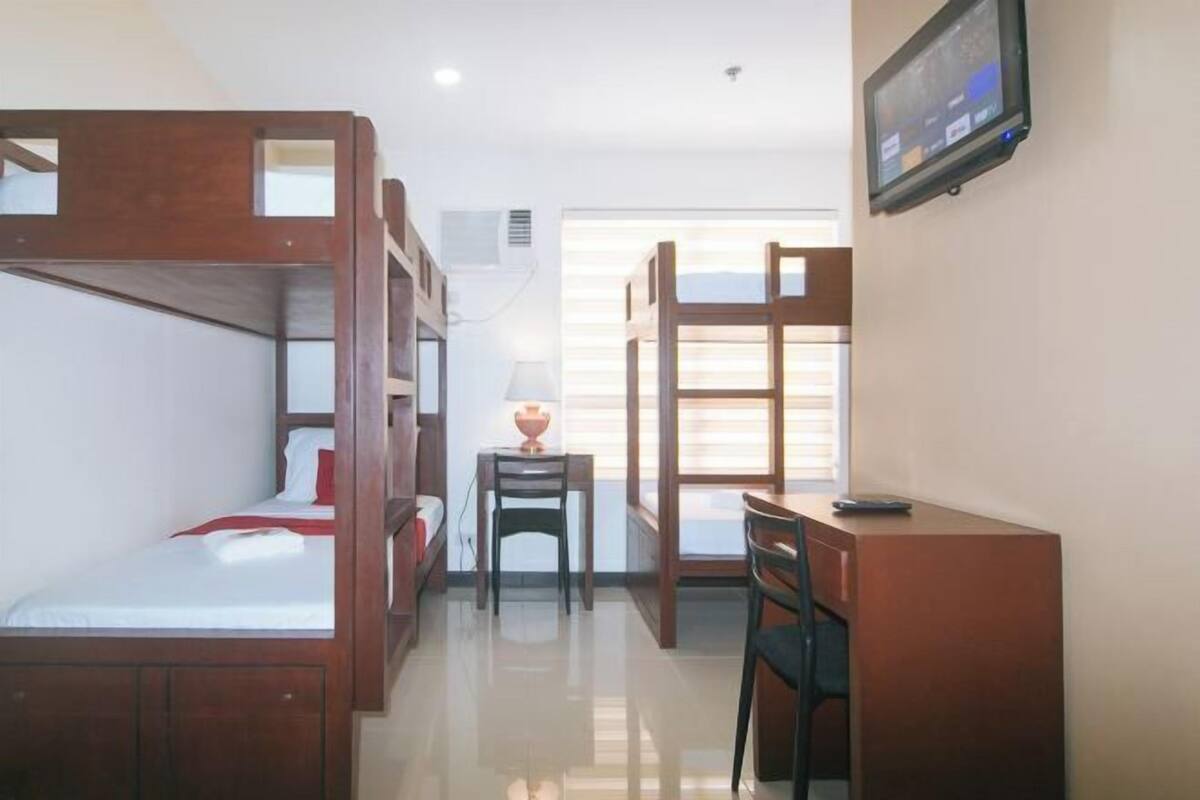 A room with bunk beds, a desk, a chair, a lamp, and a television.