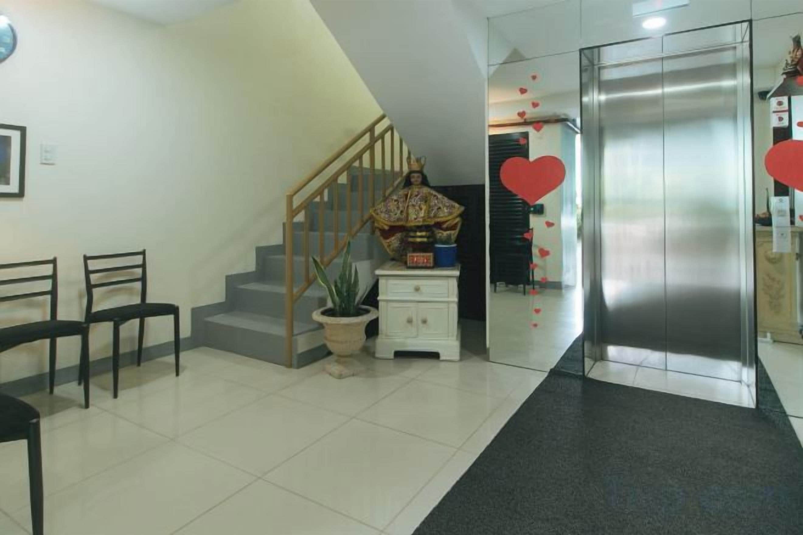 A reception area with a staircase, a potted plant, a small table, and a refrigerator.