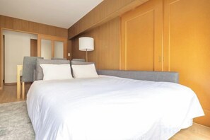 A bedroom with a large bed, a bedside table, a chair, and a lamp. - HAN HOTEL Shinjuku (Tokyo)