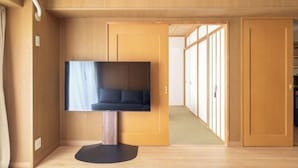 Una stanza con una TV a schermo piatto montata su un supporto, pareti e pavimento in legno, e una porta scorrevole che dà su un'altra stanza.