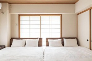 A room with two beds, wooden headboards, and a large window with a grid pattern. - HAN HOTEL Shinjuku (Tokyo)