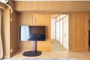 A room with a television on a stand, wooden walls, and a door leading to another room. - HAN HOTEL Shinjuku (Tokyo)