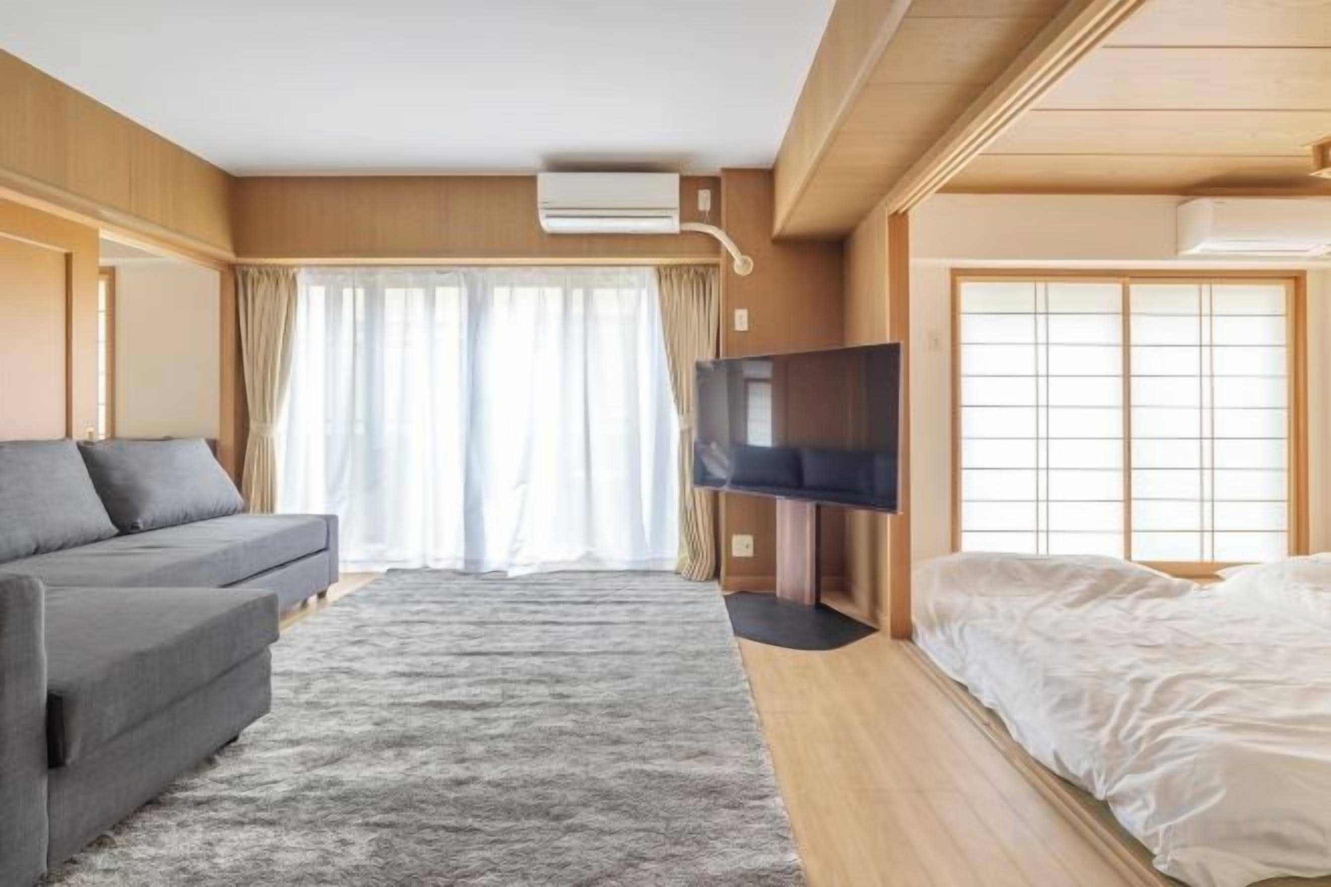 A hotel room with a sofa, a bed, a TV, and a large window with curtains.
