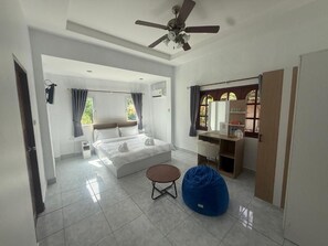 Une chambre à coucher avec un lit, un bureau, une chaise, un fauteuil poire et un ventilateur de plafond.