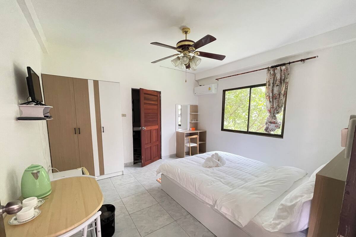 A bedroom with a bed, a desk, a wardrobe, a ceiling fan, and a window with curtains.