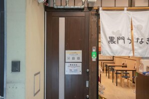 A room with a wooden door, a sign on the wall, and a banner with Japanese characters. - STAY OSAKA KUROMON Walkable to Namba, Shinsaibashi, and Dotonbori 14-minute train ride to USJ (Osaka)