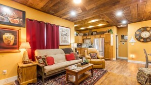 A cozy living room with a sofa, armchair, and coffee table, connected to a kitchen with wooden cabinets and a refrigerator.