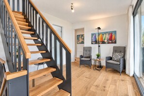 A modern interior with a wooden staircase, a seating area with two chairs, a floor lamp, and a painting of sailboats. - "LUV" House on the Shore of the Lake in Streu (Bergen auf Rügen)