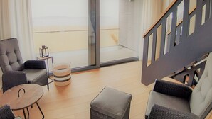 A modern living room with a sofa, armchairs, a small table, and a coffee table. There is a sliding glass door leading to a balcony with a view. - House "LUV" on the lake in Streu (Bergen auf Rügen)