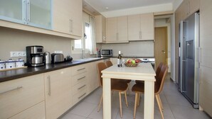 Une cuisine moderne avec des meubles en bois clair, des appareils en acier inoxydable et un coin repas comprenant une table et des chaises.