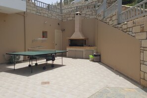 Un espace extérieur aménagé en terrasse, avec une table de ping-pong, un mur en pierre et une cheminée.