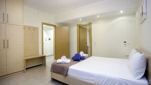 Une chambre d’hôtel avec un lit, une armoire, un banc et un miroir.