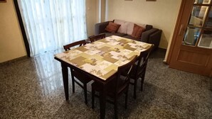 A dining area with a table and chairs, a sofa, a window with curtains, and a door with a glass panel. - Bilbilis de Mundobriga (Calatayud)