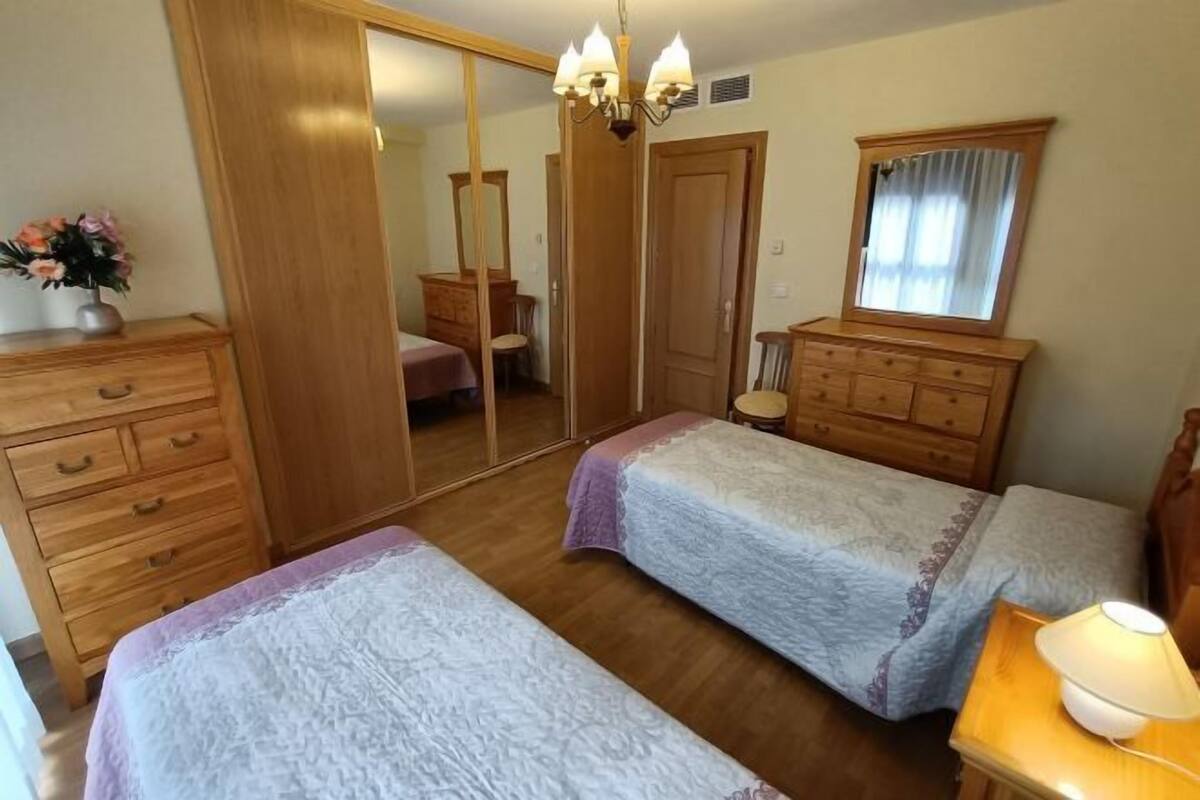 A bedroom with two beds, wooden furniture, a mirror, and a chandelier.